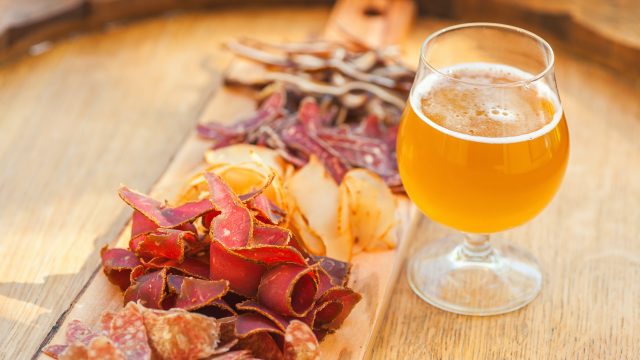 Glass of pale ale beer served with a mix of lean meat on a wooden barrel